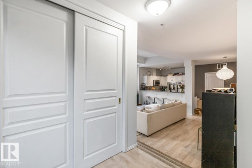 White paneled sliding doors frame a light wood-finish flooring entryway - 109 10728 82 Avenue, Edmonton, AB - Indoor Photo Showing Other Room