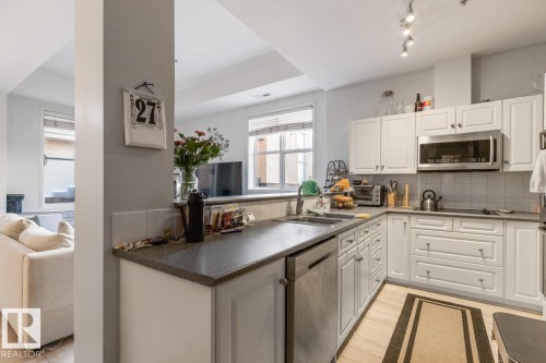Kitchen featuring white cabinetry, dark countertops, stainless steel appliances, and wood-finish flooring - 109 10728 82 Avenue, Edmonton, AB - Indoor Photo Showing Kitchen With Double Sink