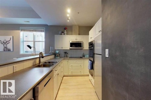 Kitchen featuring ample white cabinetry, stainless steel appliances, dual basin sink, wood-finish flooring, and track lighting - 109 10728 82 Avenue, Edmonton, AB - Indoor Photo Showing Kitchen With Double Sink