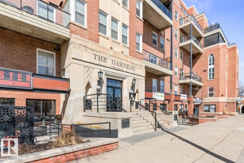 Brick-clad building facade featuring stone accents, multiple balconies with glass railings, and ground-level commercial spaces - 109 10728 82 Avenue, Edmonton, AB - Outdoor With Facade