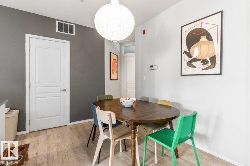 Dining area featuring wood-finish flooring, a white paneled door, and a modern pendant light fixture - 109 10728 82 Avenue, Edmonton, AB - Indoor Photo Showing Dining Room
