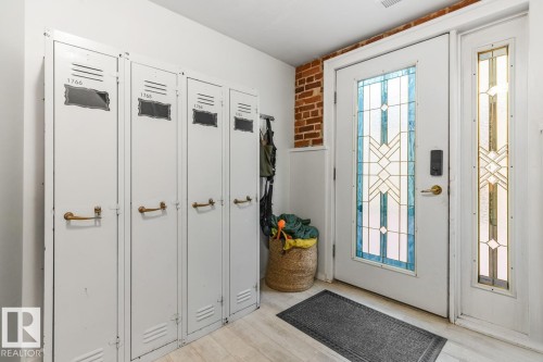 Entryway featuring a decorative glass panel door with a sidelight, exposed brick wall, light wood-finish flooring, and white wainscoting - 109 10728 82 Avenue, Edmonton, AB - Indoor Photo Showing Other Room