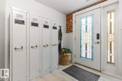 Entryway featuring a decorative glass panel door with a sidelight, exposed brick wall, light wood-finish flooring, and white wainscoting - 