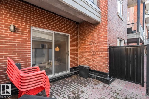 Brick patio featuring a paver surface, sliding glass door access, outdoor wall light fixture, and black privacy gate - 109 10728 82 Avenue, Edmonton, AB - Outdoor With Exterior