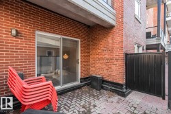 Brick patio featuring a paver surface, sliding glass door access, outdoor wall light fixture, and black privacy gate - 