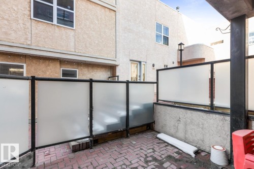 Private patio space featuring brick paver flooring, modern frosted panel fencing, and stucco exterior walls - 109 10728 82 Avenue, Edmonton, AB - Outdoor With Exterior