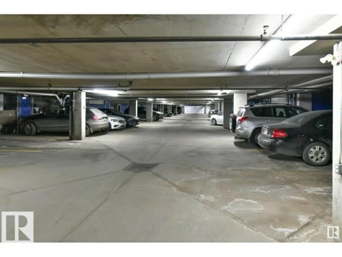 Underground parking garage featuring concrete flooring, structural columns, overhead piping, and linear fluorescent lighting fixtures - 109 10728 82 Avenue, Edmonton, AB - Indoor Photo Showing Garage