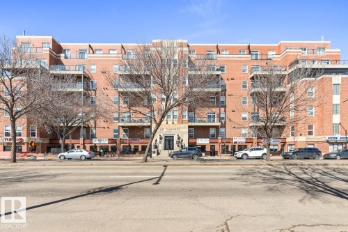 Brick multi-story building featuring multiple balconies with black railings, a stone-framed main entrance, and ground-level retail spaces - 109 10728 82 Avenue, Edmonton, AB - Outdoor