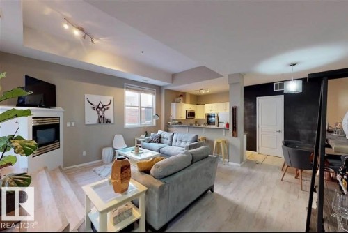 Living area featuring light wood-finish flooring, a white fireplace with a dark insert, a track lighting fixture, and a large window - 109 10728 82 Avenue, Edmonton, AB - Indoor Photo Showing Living Room