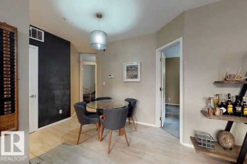 Dining area featuring wood-finish flooring, a contemporary pendant light fixture, an accent wall, and an open doorway - 109 10728 82 Avenue, Edmonton, AB - Indoor Photo Showing Dining Room