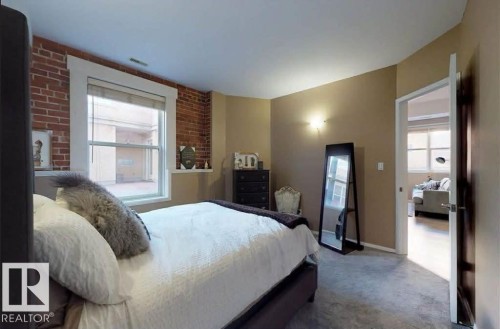 Exposed brick accent wall with a large window - 109 10728 82 Avenue, Edmonton, AB - Indoor Photo Showing Bedroom