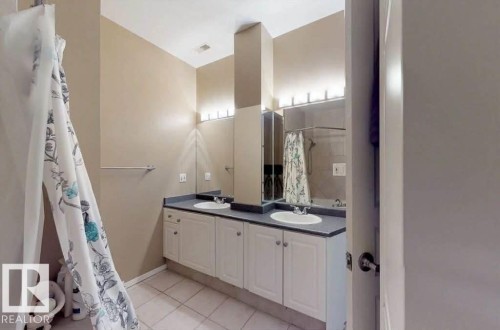 Dual vanity with white cabinetry, dark countertops, two integrated sinks, and individual wall-mounted lighting fixtures - 109 10728 82 Avenue, Edmonton, AB - Indoor Photo Showing Bathroom
