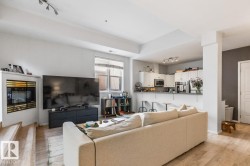 Open-concept living area featuring wood-finish flooring, a built-in fireplace, track lighting, a kitchen bar, and white cabinetry with stainless steel appliances - 