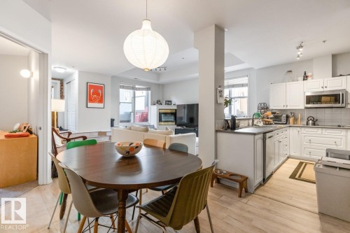Open-concept living space featuring wood-finish flooring, a contemporary pendant light fixture, a kitchen with white cabinetry, and a built-in stainless steel microwave - 109 10728 82 Avenue, Edmonton, AB - Indoor Photo Showing Dining Room