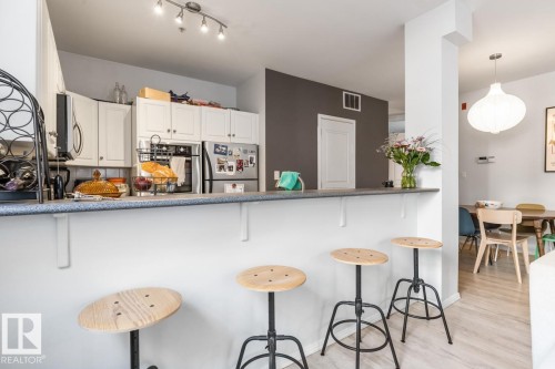 Open-concept kitchen featuring white cabinetry, stainless steel appliances, and track lighting - 109 10728 82 Avenue, Edmonton, AB - Indoor Photo Showing Kitchen