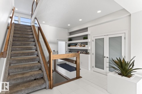Two-story foyer featuring a carpeted staircase with wood-finish railings and glass panels - 793 Windermere Wynd, Edmonton, AB - Indoor Photo Showing Other Room