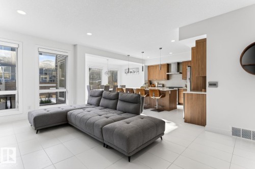 Spacious room featuring white tile flooring, recessed lighting, large windows, and an open-concept layout leading to a kitchen with wood-finish cabinetry and a kitchen island - 793 Windermere Wynd, Edmonton, AB - Indoor Photo Showing Living Room
