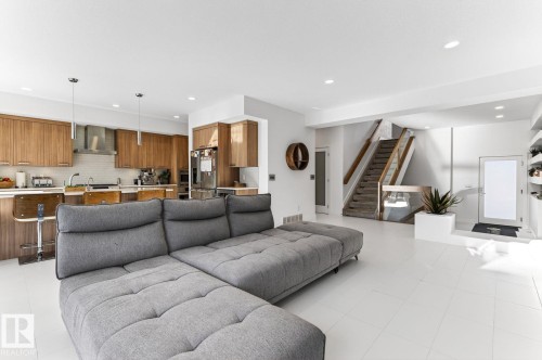 Bright open-concept interior featuring light-colored flooring, a kitchen with wood-finish cabinetry, stainless steel appliances, and a tile backsplash - 793 Windermere Wynd, Edmonton, AB - Indoor Photo Showing Living Room