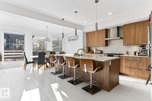 Open-concept kitchen with white tile flooring, wood-finish cabinetry, stainless steel appliances, and a central island with countertop seating - 793 Windermere Wynd, Edmonton, AB - Indoor Photo Showing Kitchen With Upgraded Kitchen
