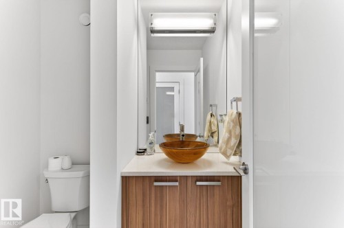 Contemporary bathroom featuring a wood-finish vanity with a vessel sink, a light-toned countertop, and a large wall-mounted mirror - 793 Windermere Wynd, Edmonton, AB - Indoor Photo Showing Bathroom