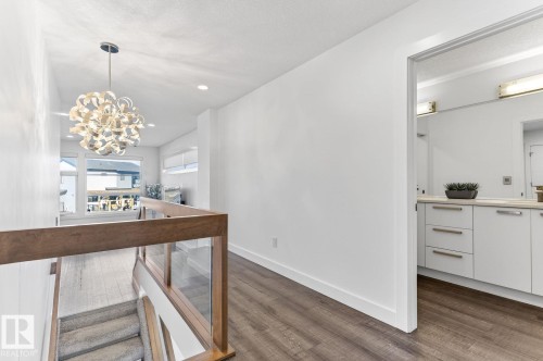 Upper-level landing featuring wood-finish flooring, a contemporary chandelier, a glass and wood-tone railing, and a window providing natural light - 793 Windermere Wynd, Edmonton, AB - Indoor Photo Showing Other Room
