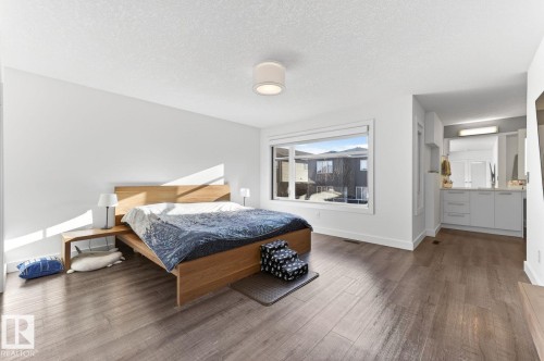 Spacious room featuring wood-finish flooring, a large window, a ceiling-mounted light fixture, and an integrated vanity area with built-in cabinetry and an illuminated mirror - 793 Windermere Wynd, Edmonton, AB - Indoor Photo Showing Bedroom