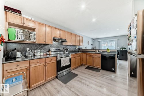 Kitchen featuring wood-finish flooring, natural wood cabinetry, dark countertops, and a tile backsplash - 715 Hudson Place, Edmonton, AB - Indoor Photo Showing Kitchen With Double Sink