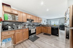 Kitchen featuring wood-finish flooring, natural wood cabinetry, dark countertops, and a tile backsplash - 