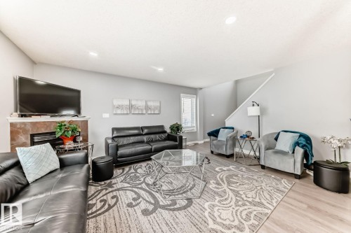 Living area featuring wood-finish flooring, recessed lighting, and a fireplace with a stone surround - 715 Hudson Place, Edmonton, AB - Indoor Photo Showing Living Room