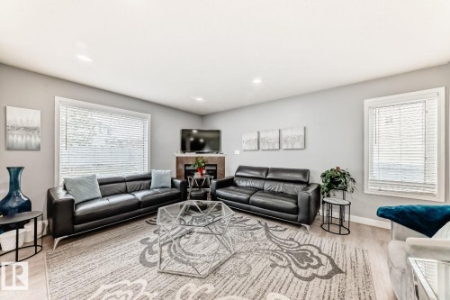 Spacious living area featuring light wood-finish flooring, a contemporary fireplace with a stone surround, recessed lighting, and large windows with horizontal blinds - 715 Hudson Place, Edmonton, AB - Indoor Photo Showing Living Room