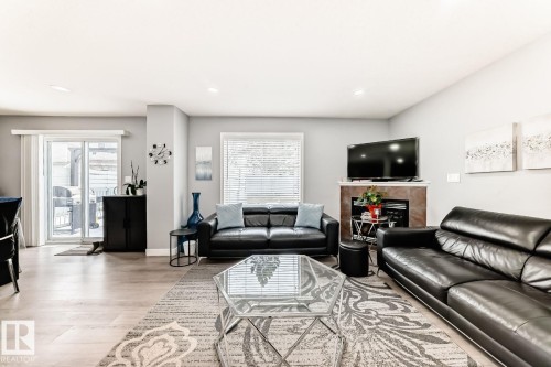 Spacious living area featuring light wood-finish flooring, a contemporary fireplace with tile surround, and a large window with blinds - 715 Hudson Place, Edmonton, AB - Indoor Photo Showing Living Room With Fireplace