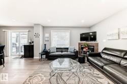 Spacious living area featuring light wood-finish flooring, a contemporary fireplace with tile surround, and a large window with blinds - 
