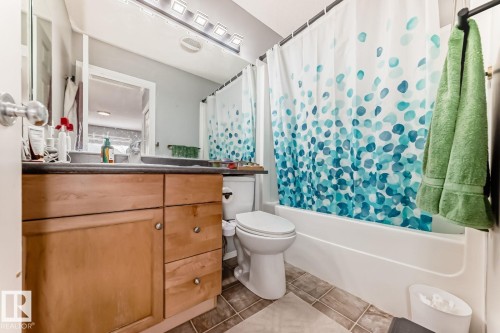 Bathroom featuring a light wood-finish vanity with a dark countertop, an integrated sink, a white toilet, a white tub, and tile flooring - 715 Hudson Place, Edmonton, AB - Indoor Photo Showing Bathroom