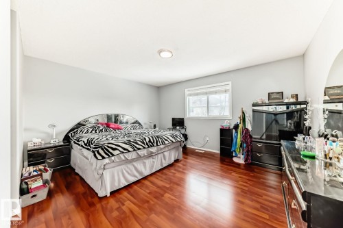 Spacious room featuring rich wood-finish flooring, light gray walls, a ceiling-mounted light fixture, and a large window with white trim - 715 Hudson Place, Edmonton, AB - Indoor Photo Showing Bedroom