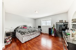 Spacious room featuring rich wood-finish flooring, light gray walls, a ceiling-mounted light fixture, and a large window with white trim - 