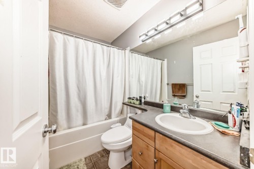 Bathroom featuring a tub/shower combination with white surround, a toilet, a vanity with wood-finish cabinetry, a single basin sink, and a large wall-mounted mirror - 715 Hudson Place, Edmonton, AB - Indoor Photo Showing Bathroom