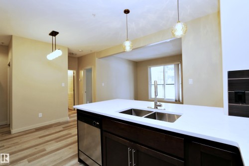 Kitchen island featuring a white solid surface countertop with an undermount double-basin stainless steel sink and a stainless steel dishwasher - 140 308 Ambleside Link Link Sw, Edmonton, AB - Indoor Photo Showing Kitchen With Double Sink