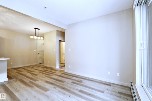 Open-concept living area featuring wood-finish flooring, a modern linear chandelier, and a sliding glass door providing natural illumination - 140 308 Ambleside Link Link Sw, Edmonton, AB - Indoor Photo Showing Other Room