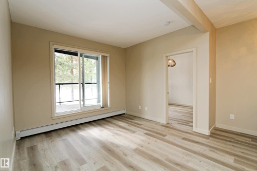 Spacious room featuring wood-finish flooring, neutral paint palette, and a sliding glass door leading to an outdoor space - 140 308 Ambleside Link Link Sw, Edmonton, AB - Indoor Photo Showing Other Room
