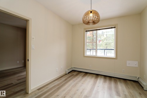 Bright room featuring wood-finish flooring, a modern spherical pendant light fixture, and a window with a dark frame - 140 308 Ambleside Link Link Sw, Edmonton, AB - Indoor Photo Showing Other Room