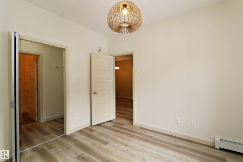 Neutral-toned interior featuring wood-finish flooring, a modern decorative light fixture, and white trim - 140 308 Ambleside Link Link Sw, Edmonton, AB - Indoor Photo Showing Other Room