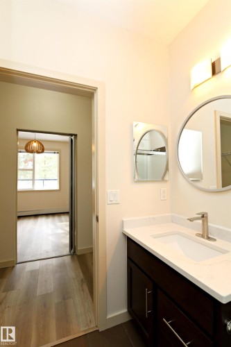 Bathroom vanity featuring a white Quartz countertop with integrated sink, dark wood-finish cabinetry, and brushed nickel hardware - 140 308 Ambleside Link Link Sw, Edmonton, AB - Indoor Photo Showing Bathroom