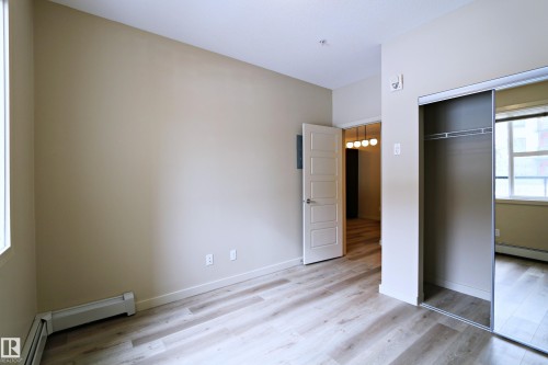 Neutral-toned room featuring light wood-finish flooring, a white five-panel interior door, and a built-in closet with mirrored sliding doors - 140 308 Ambleside Link Link Sw, Edmonton, AB - Indoor Photo Showing Other Room