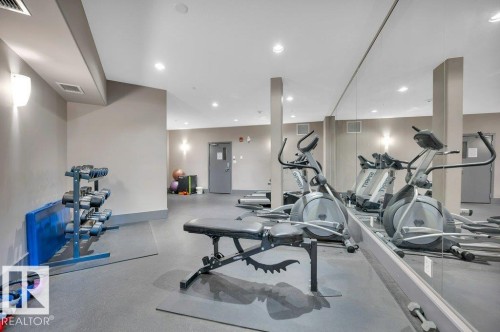 Fitness room featuring cushioned rubber flooring, mirrored wall, recessed lighting, wall sconces, and exercise equipment - 140 308 Ambleside Link Link Sw, Edmonton, AB - Indoor Photo Showing Gym Room