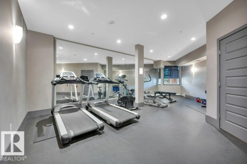 Fitness room featuring resilient flooring, recessed lighting, mirrored walls, and a paneled door - 140 308 Ambleside Link Link Sw, Edmonton, AB - Indoor Photo Showing Gym Room