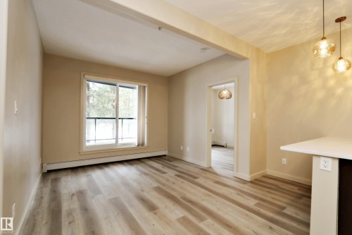Spacious living area featuring wood-finish flooring, a large window, and warm neutral wall tones - 140 308 Ambleside Link Link Sw, Edmonton, AB - Indoor Photo Showing Other Room
