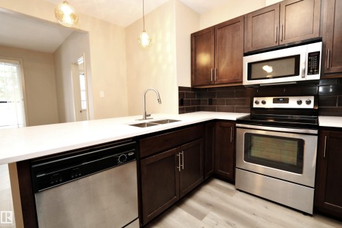 Kitchen featuring dark wood cabinetry, white countertops, a stainless steel appliance suite, subway tile backsplash, and light wood-finish flooring - 140 308 Ambleside Link Link Sw, Edmonton, AB - Indoor Photo Showing Kitchen With Double Sink