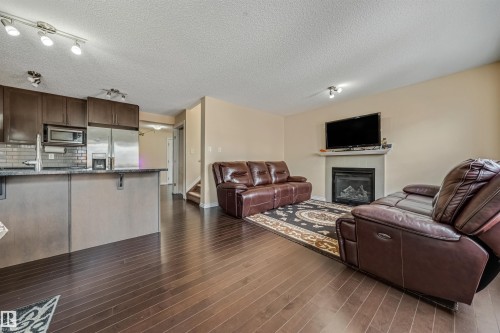 Open-concept living space featuring wood-finish flooring, a kitchen island with dark cabinetry, stainless steel appliances, a tile backsplash, and a gas fireplace with a mantel - 2314 22 Avenue, Edmonton, AB - Indoor With Fireplace