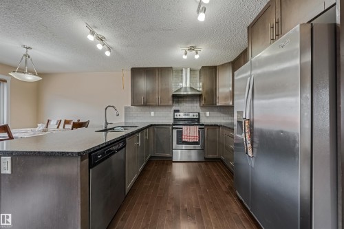 Modern kitchen featuring dark wood-finish cabinetry, stainless steel appliances, dark stone countertops, and wood-finish flooring - 2314 22 Avenue, Edmonton, AB - Indoor Photo Showing Kitchen With Upgraded Kitchen
