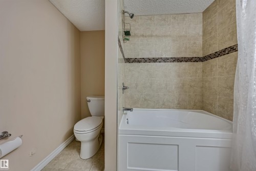 Full bathroom featuring a tiled shower/bathtub combination with decorative accent band, a white toilet, and neutral wall tones - 2314 22 Avenue, Edmonton, AB - Indoor Photo Showing Bathroom